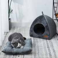 Thumbnail for A gray cat lounges on a gray cushion near the KittyNook Cat Co. Cozy Triangle Cat Cave Bed in a modern room.