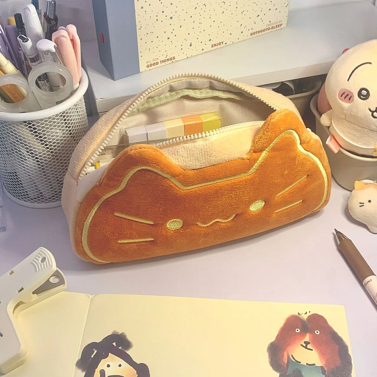 The Caramel Cat Plush Pencil Case by KittyNook Cat Co. sits on a desk with pens and school supplies.