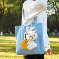 Thumbnail for Person carries a blue KittyNook Cat Co. crossbody cat carrier bag with a bunny design and a white cat’s head visible.