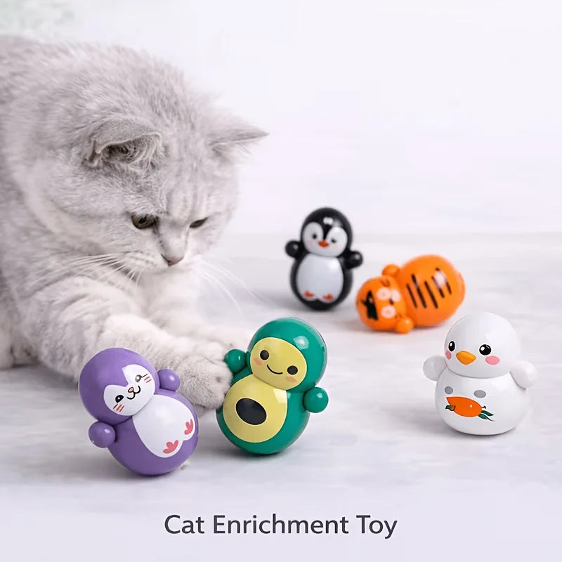 A cat bats at a group of small, rounded, cartoon-style Cat Rolling Toy Set – Self-Rolling Interactive Cat Toys.