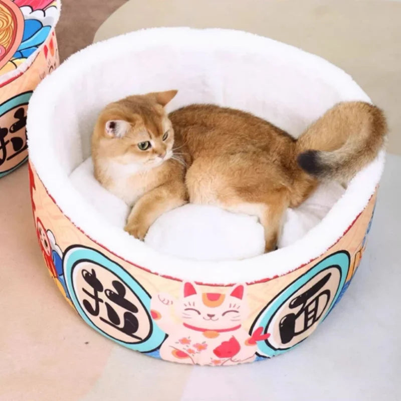 A light brown cat lounges in a Giant Ramen Bowl Cat Bed by KittyNook Cat Co., featuring cartoon and Asian designs.