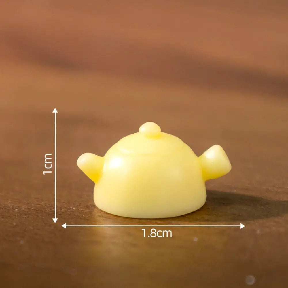 A 1cm yellow teapot sits beside the KittyNook Cat Co. Creative Cat Doll Car Ornament on a wooden surface.