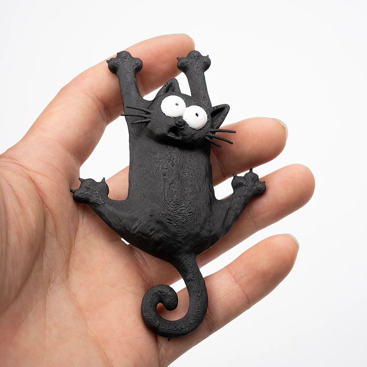 A hand holds a KittyNook Cat Co. Hanging Kitty Magnetic Fridge Decor, a playful black cat magnet with wide eyes.