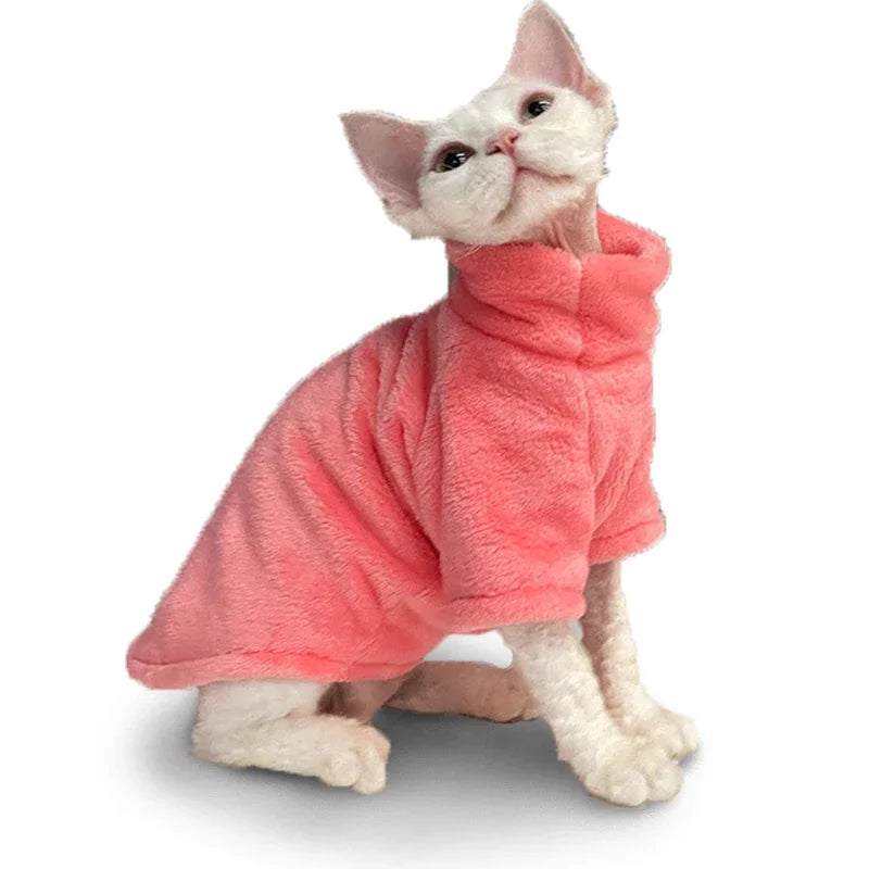 A white cat models the KittyNook Cat Co. Warm Winter Hoodie for Hairless Kittens in soft pink, looking up on white.
