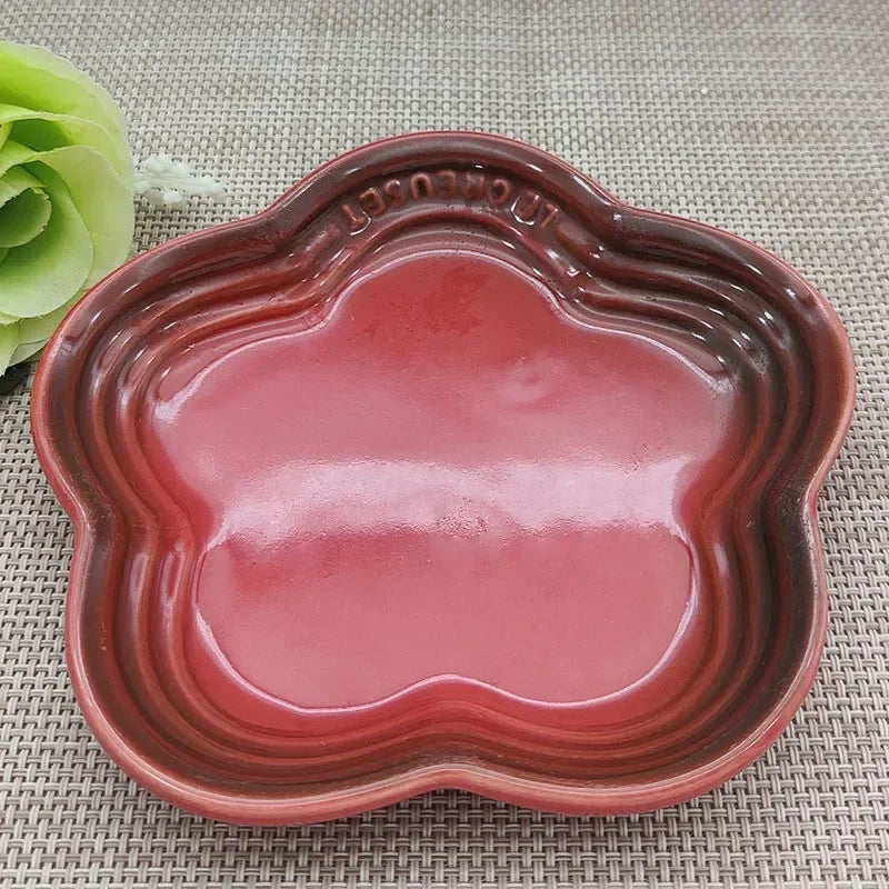 KittyNook Cat Co.'s Extra Wide Raised Flower Cat Bowl, red and scalloped, sits on a placemat beside a green flower.