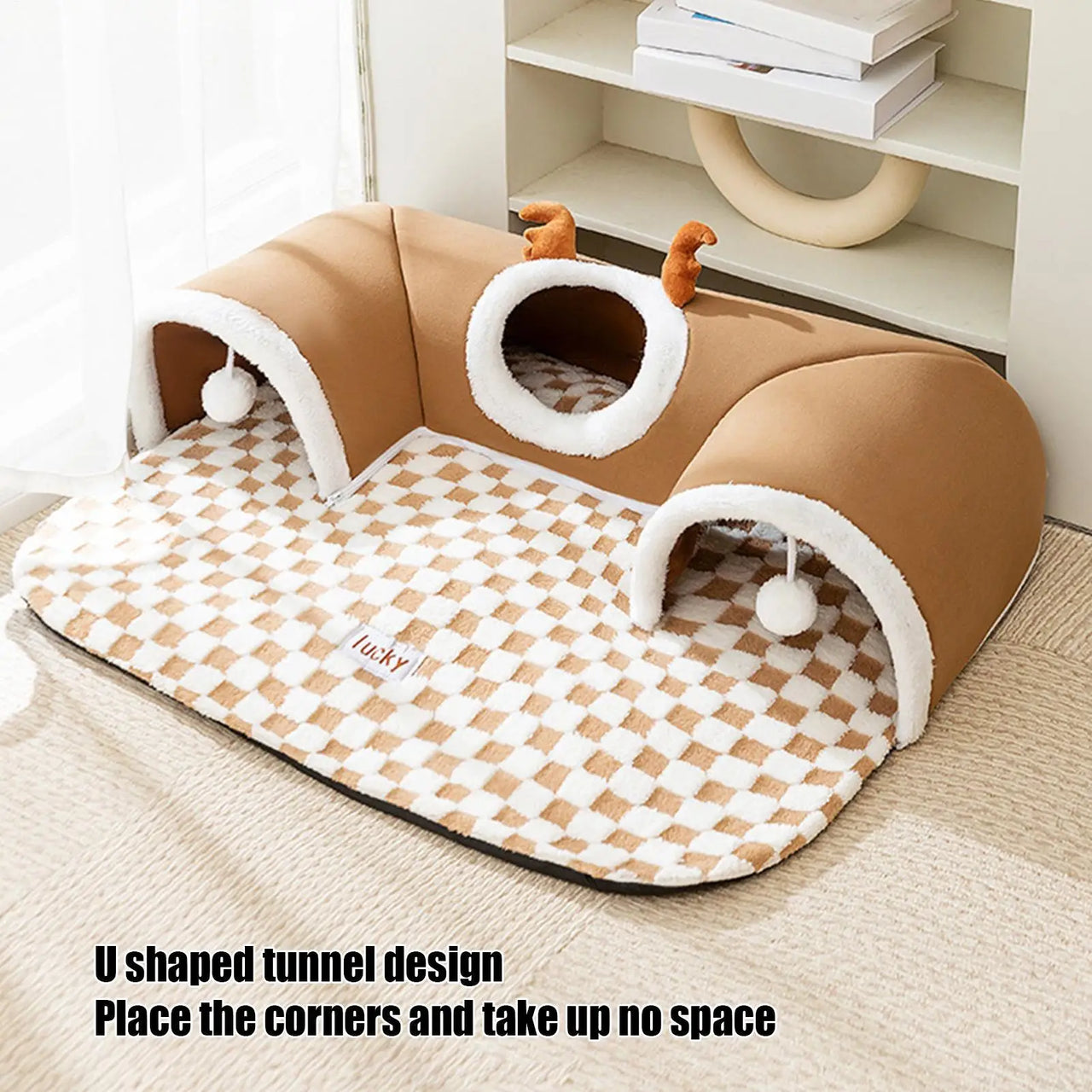 The KittyNook Cat Co. Winter Warm Plush Tunnel Cat Bed with toys sits on a checkered mat near shelves and a window.