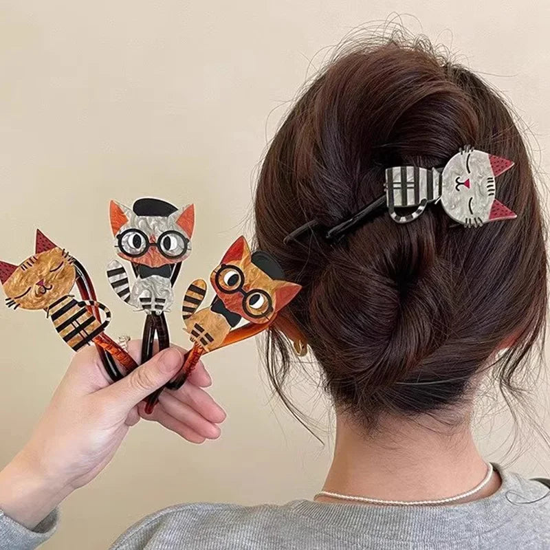 A person wears The Acrylic Cat Hairpin by KittyNook Cat Co., holding three colorful cat hair accessories.