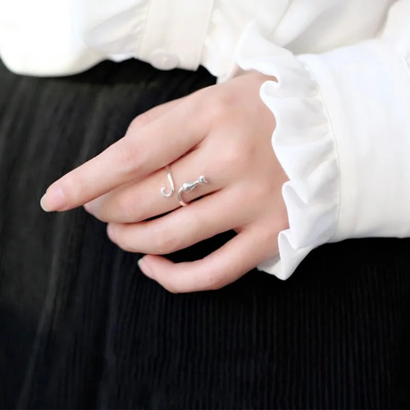 A hand wears the KittyNook Cat Co. Cute Adjustable Silver Cat Ring, paired with a white ruffled sleeve and black skirt.