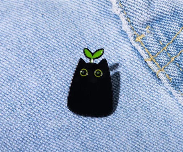 KittyNook Cat Co.'s Black Cat Enamel Brooch with green eyes and a sprout is perfect for enamel jewelry lovers.