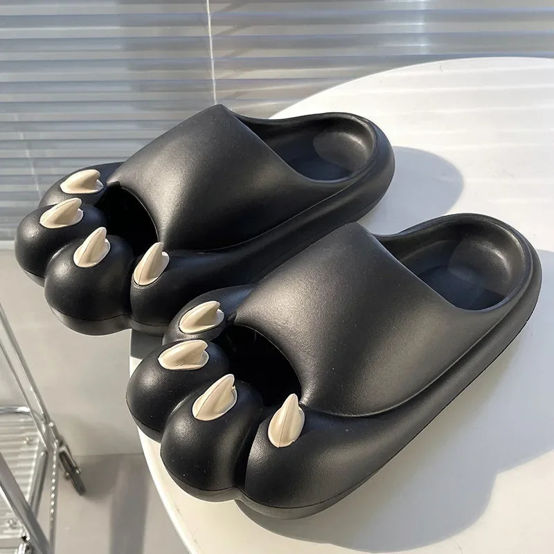 Comfy Outdoor Cat Slippers by KittyNook Cat Co. feature black slides with beige cat claws, shown on a white round table.