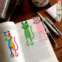 Thumbnail for Three Sleek Flat Cat Acrylic Bookmarks by KittyNook Cat Co. rest on an open book beside pens and a notebook.
