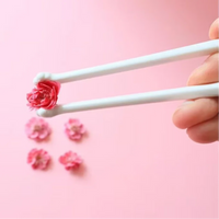Thumbnail for KittyNook Cat Co. Little Paws Silicone Training Chopsticks for Kids hold a pink flower, with more on a pink background.