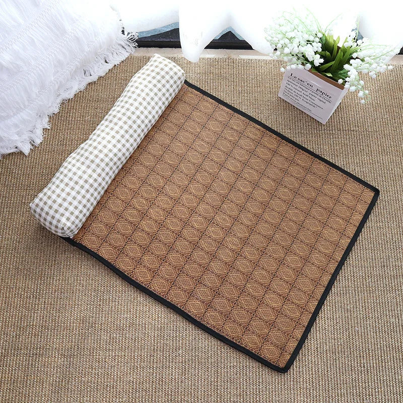 The KittyNook Cat Co. Natural Rattan Cat Sleeping Mat with checkered pillow sits on a carpet by a plant and white blanket.