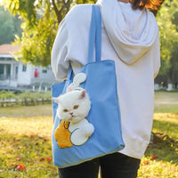 Thumbnail for A white cat lounges in a KittyNook Cat Co. Portable Crossbody Cat Carrier Bag, carried by someone in a white hoodie.
