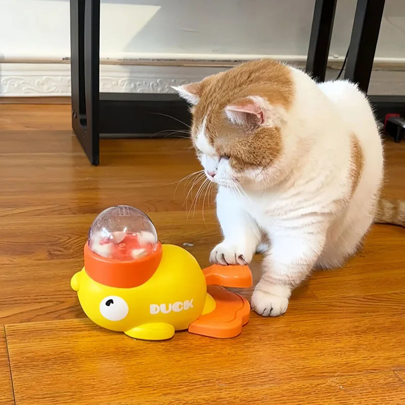 A cat taps a yellow KittyNook Cat Co. Non-Toxic Pet IQ Food Leak Tumbler on a wooden floor.
