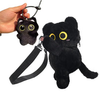 Thumbnail for A hand holds a black plush cat keychain beside KittyNook Cat Co.'s Cute Big Eyes Plush Backpack with a handy strap.