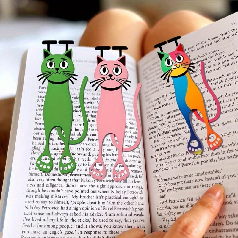Three Sleek Flat Cat Acrylic Bookmarks by KittyNook Cat Co. clip onto a book held in someone’s hand.
