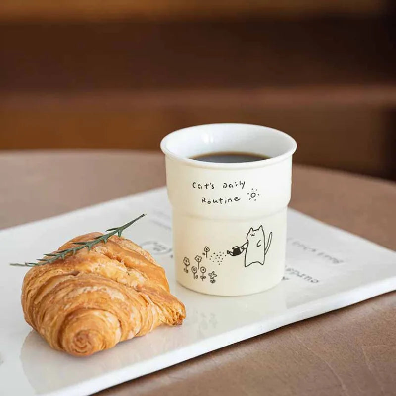 A croissant and coffee in a KittyNook Cat Co. Cute Illustrated Ceramic Cat Mug on a white tray.