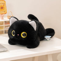 Thumbnail for The Cute Big Eyes Kitten Stuffed Animal Plush Pillow by KittyNook Cat Co. lies on a white desk in a bright room.