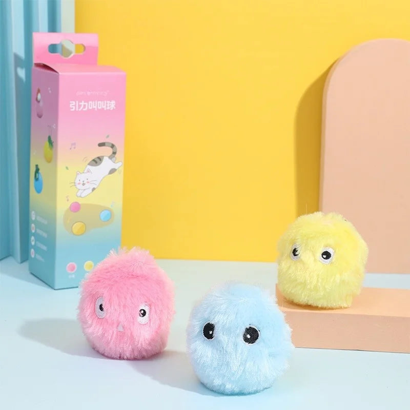 Three fluffy KittyNook Cat Co. balls with eyes sit by a box—perfect as Interactive Cat Smart Ball Toys.