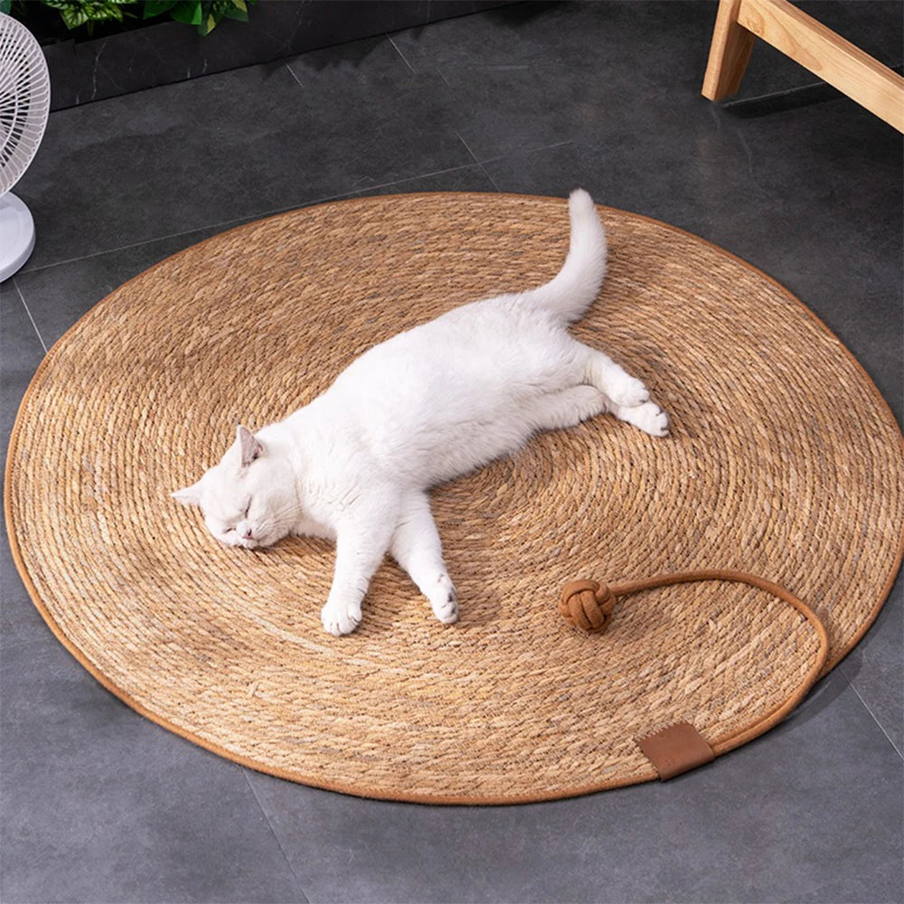 A white cat relaxes on a KittyNook Cat Co. Natural Rattan Cat Scratcher, enjoying comfort on a gray tile floor.