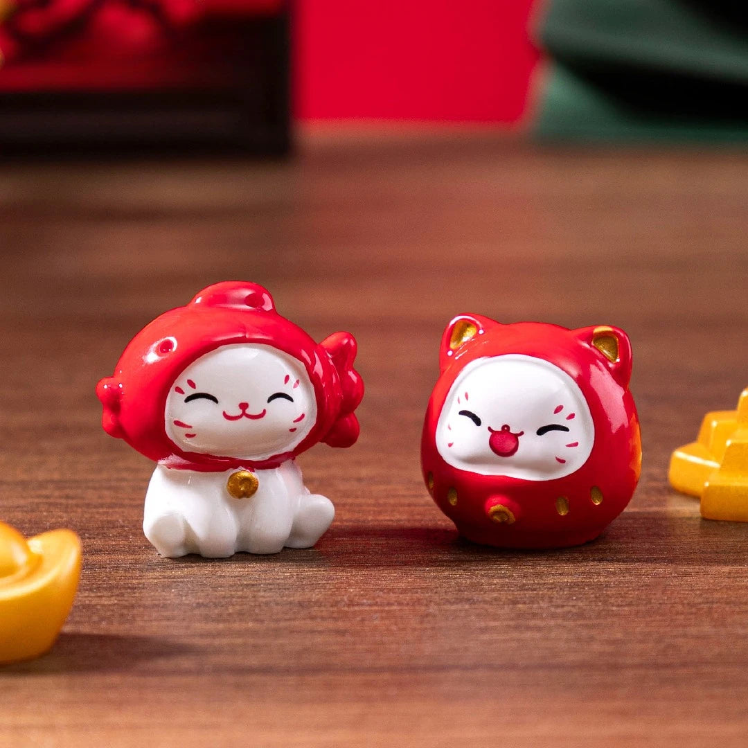 Two Chinese Cartoon Fortune Cat Ornaments by KittyNook Cat Co. with red capes sit on a surface beside gold ingot decor.