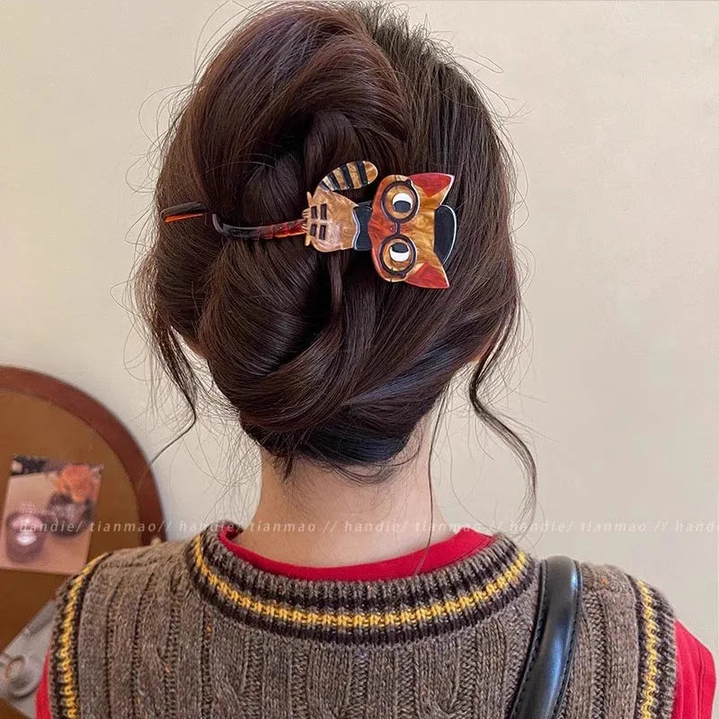 Woman with a brown bun, styled with KittyNook Cat Co.’s The Acrylic Cat Hairpin, wears a brown vest with red trim.