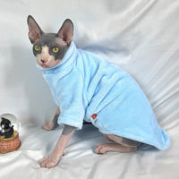 Thumbnail for A hairless kitten in a Warm Winter Hoodie by KittyNook Cat Co. sits on a white surface beside a cat snow globe.