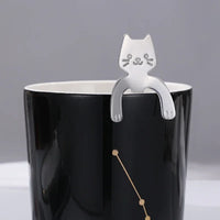 Thumbnail for The KittyNook Cat Co. Cat Cling Stainless Steel Mug Spoon hangs on a black mug with a gold constellation design.