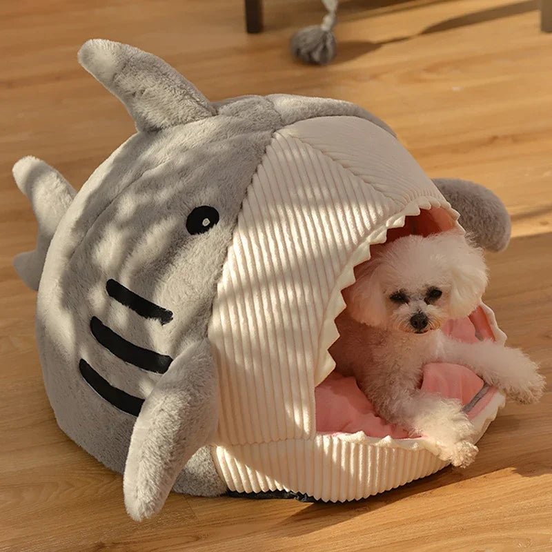 A small white dog lounges in a KittyNook Cat Co. Shark-Shaped Cat Cave Bed on a wooden floor.
