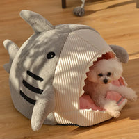 Thumbnail for A small white dog lounges in a KittyNook Cat Co. Shark-Shaped Cat Cave Bed on a wooden floor.
