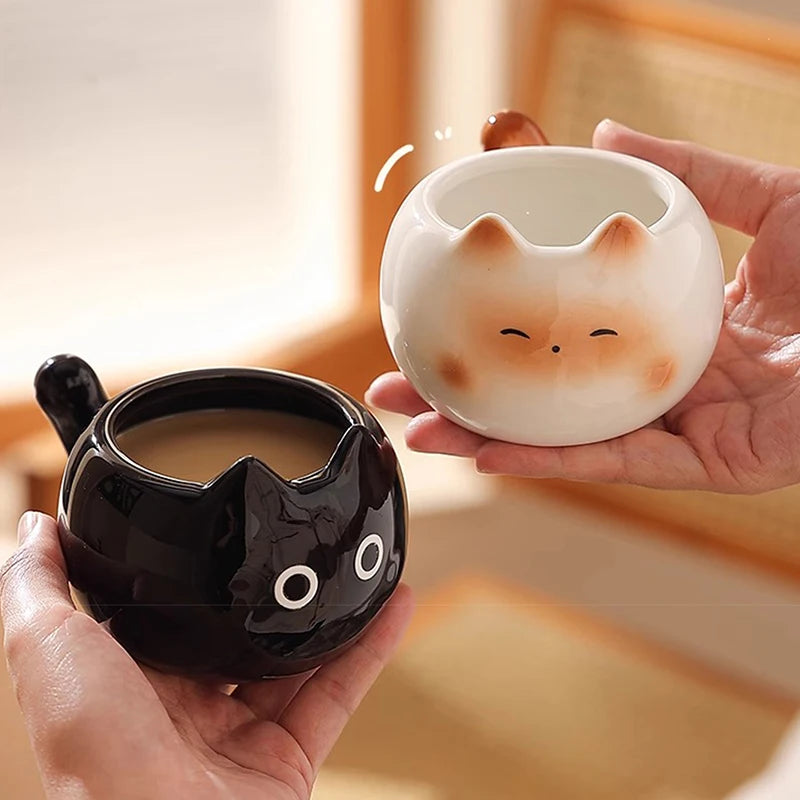 Two hands hold KittyNook Cat Co.'s Siamese Cat Coffee Cup and a cat lovers mug in a cozy, cat-themed setting.
