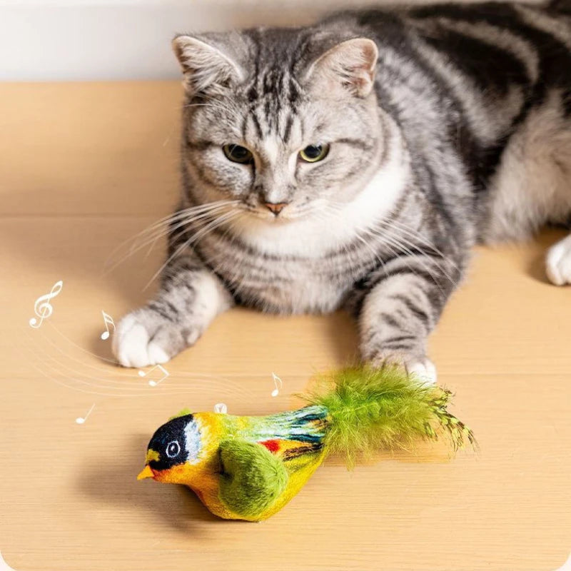 A gray tabby on a wooden floor plays with KittyNook Cat Co.'s Ultimate Interactive Chirping Bird Cat Toy.