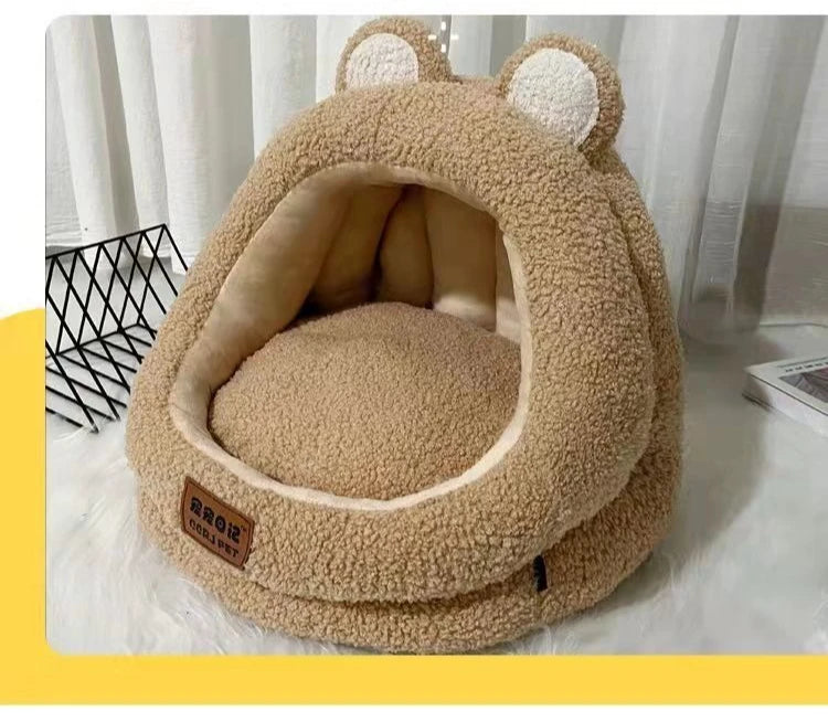 A cozy tan KittyNook Cat Co. Ultra Soft Cat Nest with bear ears sits on a white floor near curtains and a book.