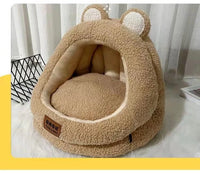 Thumbnail for A cozy tan KittyNook Cat Co. Ultra Soft Cat Nest with bear ears sits on a white floor near curtains and a book.