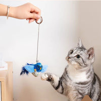 Thumbnail for A grey tabby reaches for a KittyNook Cat Co. Ultimate Interactive Chirping Bird Cat Toy held above a wooden table.