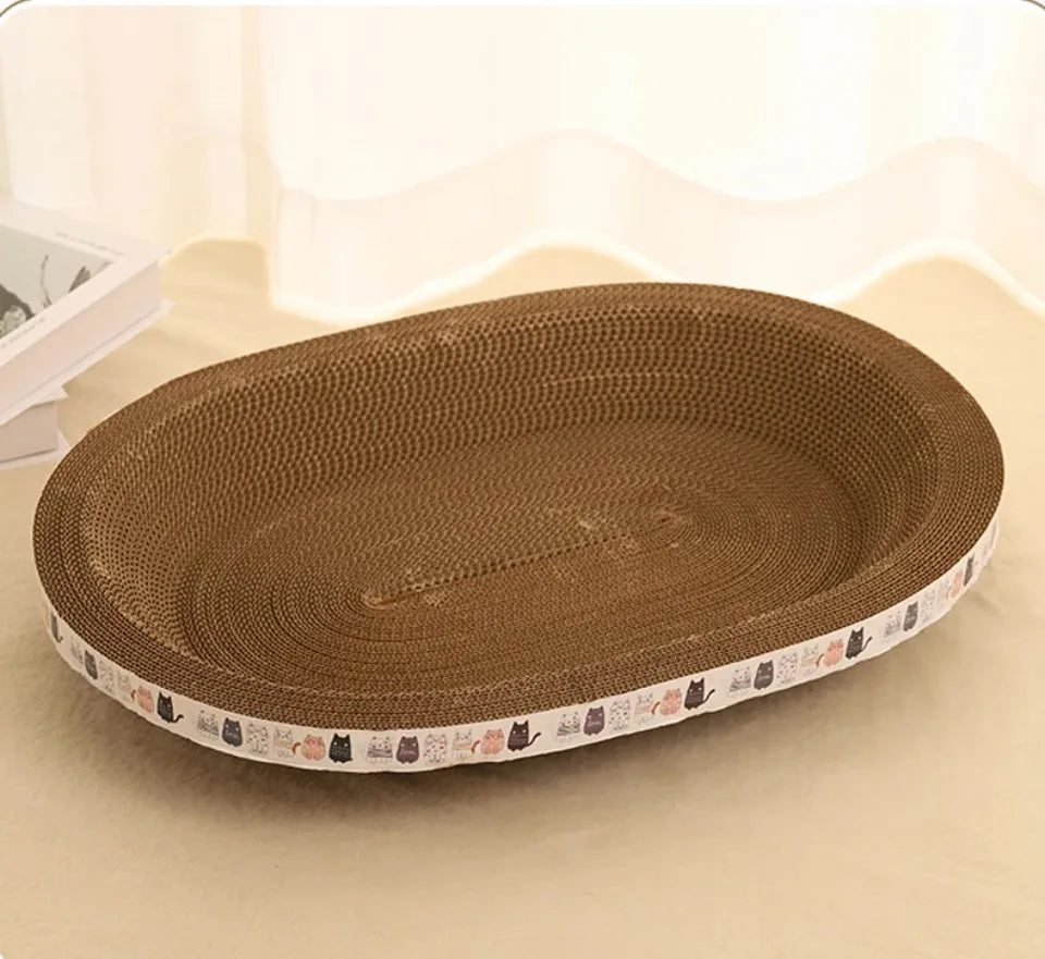 KittyNook Cat Co. Oval Corrugated Cat Scratching Board with cartoon cats on the edge, shown on a beige surface.
