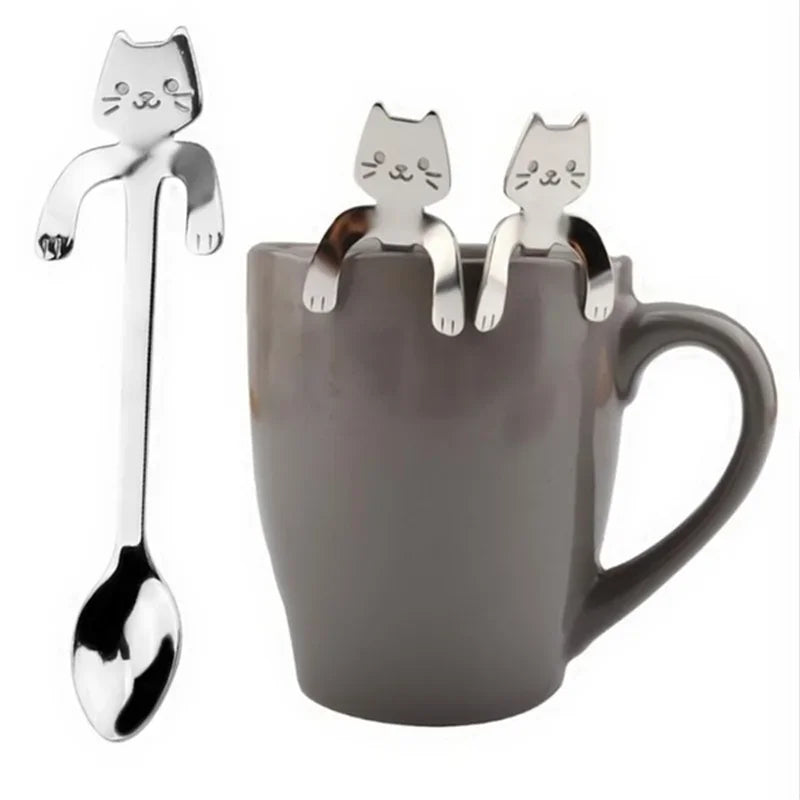 Two KittyNook Cat Co. Cat Cling Stainless Steel Mug Spoons rest on a gray mug, one shown separately on the left.
