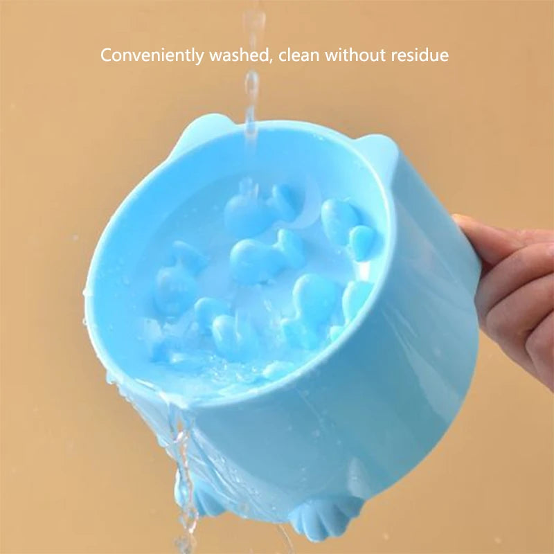 A hand rinses the blue KittyNook Cat Co. Elevated Anti-Choke Slow Feeder Bowl under running water with text above.