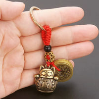 Thumbnail for A hand holds the KittyNook Cat Co. Lucky Paws Fortune Cat Keychain, featuring red string, bead, and coin charm.