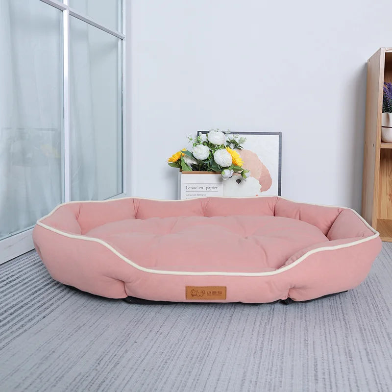 The Comfy Cat Sofa Sleeping Bed by KittyNook Cat Co. sits on a gray carpet near a window with flowers and a picture nearby.