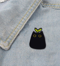 Thumbnail for The KittyNook Cat Co. Black Cat Enamel Brooch brightens a denim jacket with yellow eyes and green leaf ears.