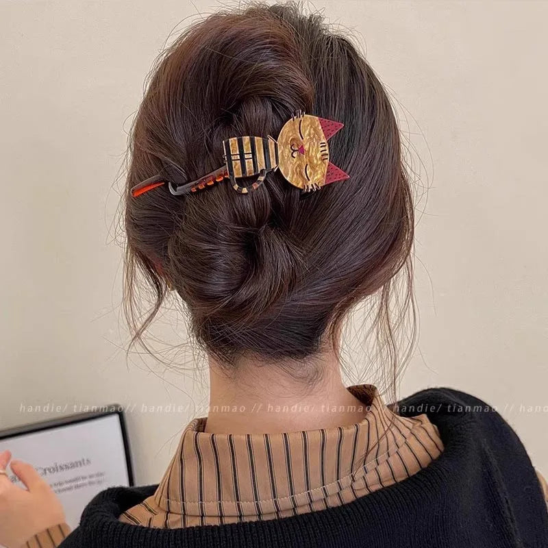 A woman with brown hair in a bun wears The Acrylic Cat Hairpin by KittyNook Cat Co. in a casual indoor setting.