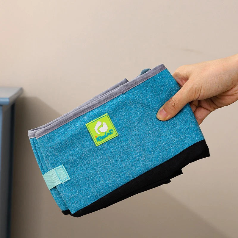 Hand holding a folded KittyNook Cat Co. Portable Cat Litter Box with green logo patch and velcro strap.