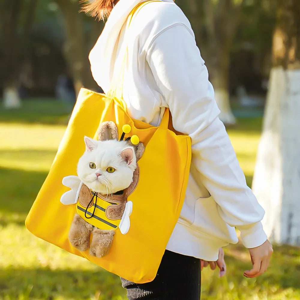 A white cat in a bee costume sits in a yellow KittyNook Cat Co. Portable Crossbody Cat Carrier Bag, held by someone.