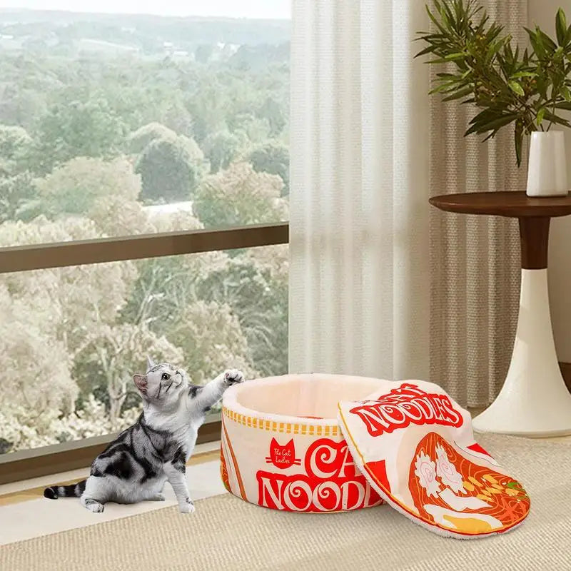 A gray tabby kitten plays beside a KittyNook Cat Co. Cute Ramen Cat Bed, adding ramen bowl charm to the bright room.