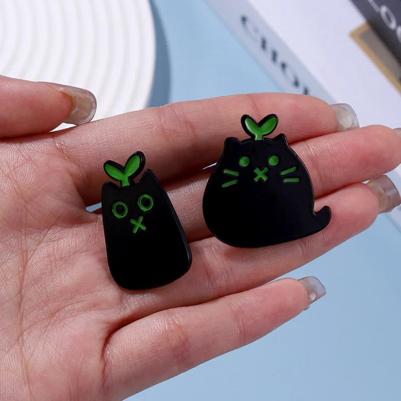 Two Black Cat Enamel Brooches by KittyNook Cat Co. with green leaves—playful pins for any cat lover.