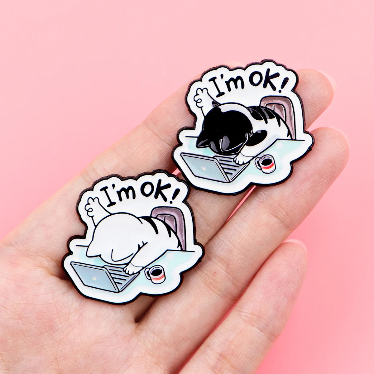 The Cat at Work Enamel Brooch Pin by KittyNook Cat Co. lies on a laptop, making a cute office accessory.