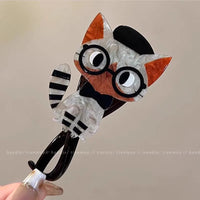Thumbnail for A hand holds The Acrylic Cat Hairpin by KittyNook Cat Co.—a cute striped cat hair accessory with glasses and a bow tie.