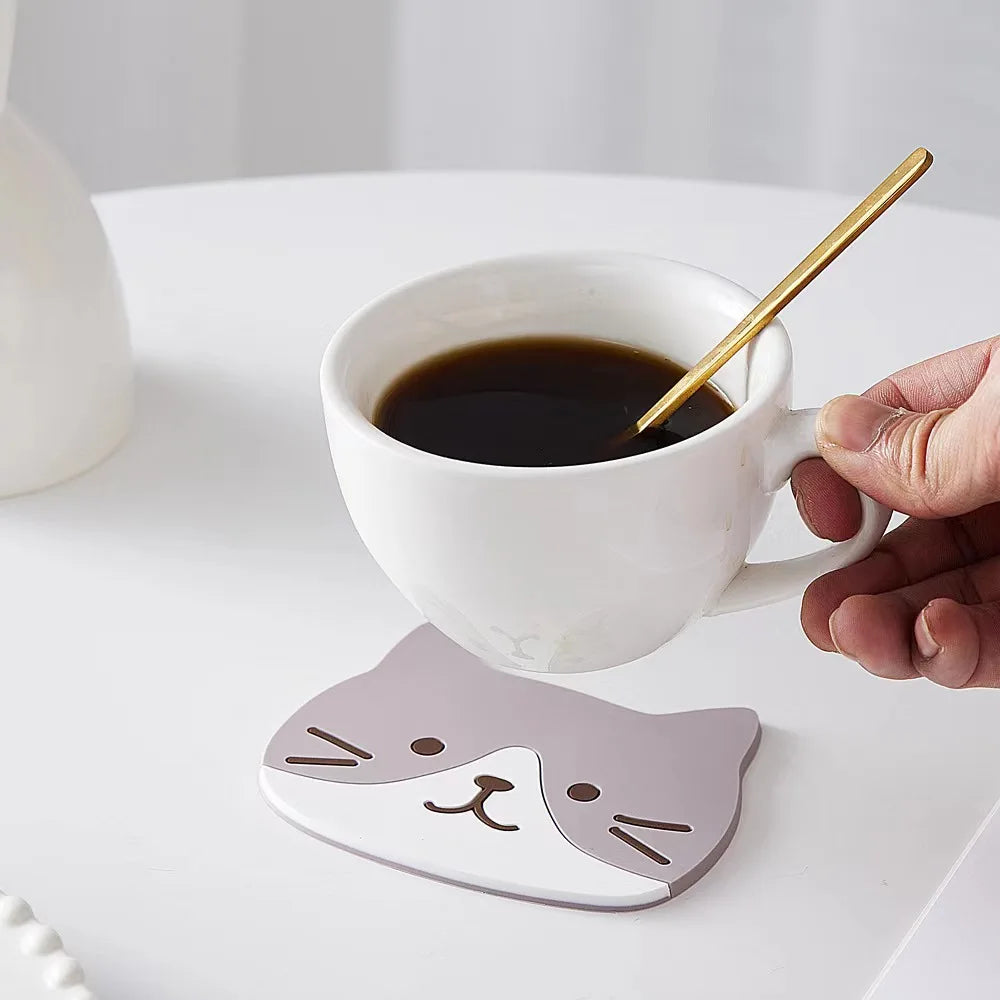Hand holding coffee with a gold spoon on KittyNook Cat Co.'s Cat Silicone Cup Coaster Mat, heat-resistant and non-slip.